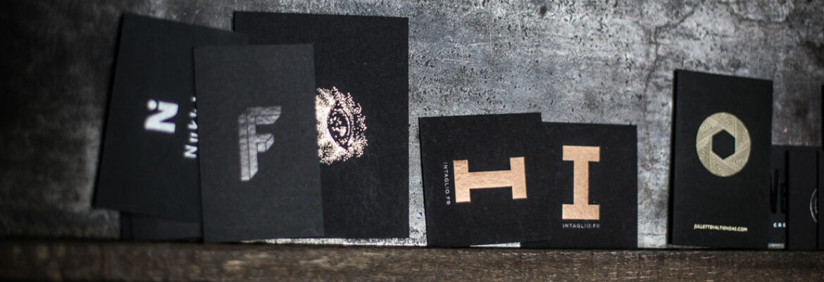 Une photo qui représente un linéaire de cartes de visite noires avec des dorures noires, argent, or, bronze, sur un meuble d'atelier