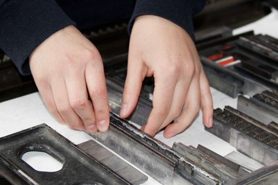 Cette image montre les mains de Anne-Laure, occupée à caler ses éléments typographiques dans un cadre dédié à un projet d'affiche qui sera imprimé sur la presse à épreuve d'Intaglio.